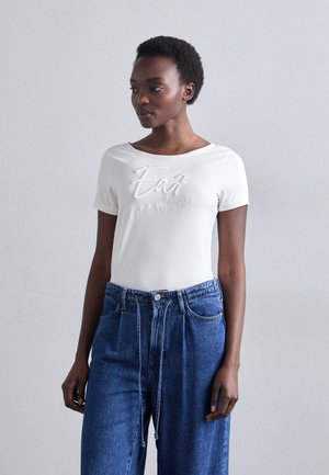 Hvit t-skjorte med korte ermer har brodert "Eat"-tekst i kontrastfarge, kombinert med løse, blå denimjeans med justerbart snor i livet.