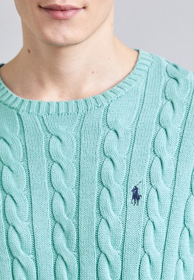 Pull en maille torsadée vert menthe avec encolure côtelée et un discret patch logo marine. Présente des motifs texturés et une coupe ajustée.