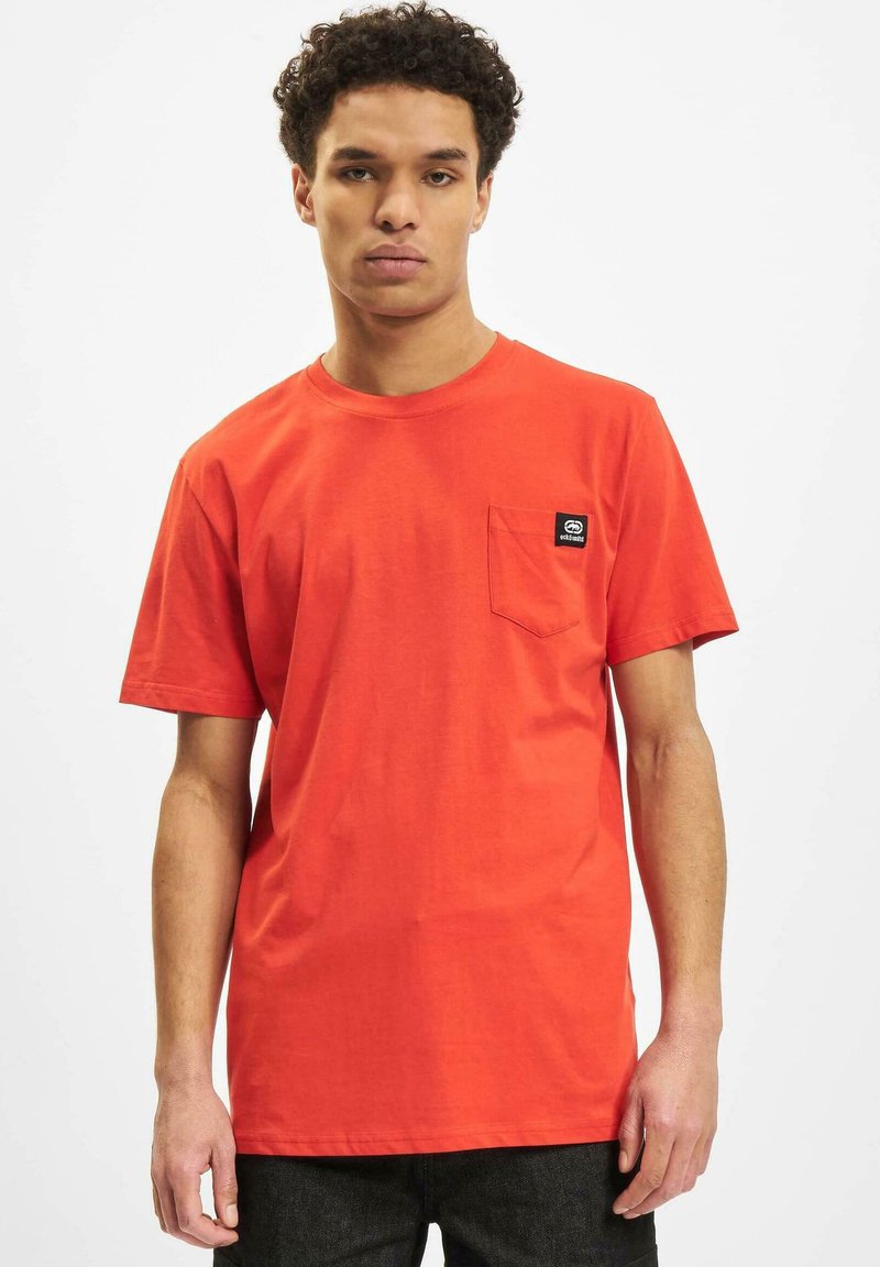 Rotes Baumwoll-T-Shirt mit Rundhalsausschnitt, kurzen Ärmeln und einer kleinen Brusttasche auf der linken Seite, die mit einem kleinen schwarzen Logolabel versehen ist. Einfaches Design, legere Passform.