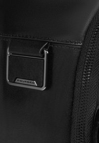 Zwarte leren tashoek met een zilverkleurige metalen ring en ritssluiting. Het materiaal heeft een gladde textuur met stikdetails.