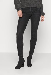Jeans negros ajustados de mezclilla, con una forma entallada, ligero estiramiento y un acabado limpio en el tobillo, combinados con botas negras de tacón.
