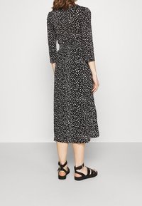 Czarna midi sukienka w białe abstrakcyjne plamy, z marszczonym pasem i rękawami o długości trzech czterech. W zestawie z czarnymi sandałami na płaskiej podeszwie z paskami.