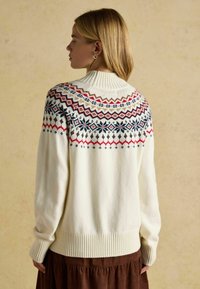 Krémový pletený sveter s rebrovaným golierom a manžetami. Obsahuje vzorovaný jho v námorníckej modrej, červenej a hnedej farbe, so geometrickými vzormi.