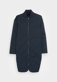 Giacca trapuntata blu notte con colletto rialzato, chiusura frontale con zip e tasca quadrata sul petto. Presenta un design fino al ginocchio e una texture morbida.