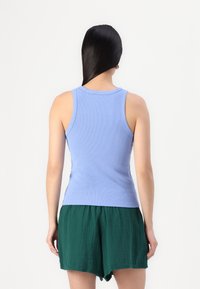 Ljusblå ribbad linne med rund halsringning och ärmlös design, kombinerad med gröna shorts, visad bakifrån.