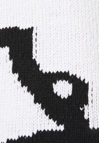 Tessuto lavorato a maglia in bianco e nero con un audace motivo astratto, caratterizzato da texture contrastanti di punti lisci e in rilievo.
