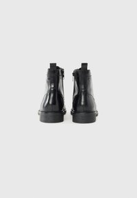 Botas de tobillo de cuero negro con un acabado suave, cremalleras laterales y un tacón bajo apilado. Presentan lengüetas en la parte posterior para facilitar el uso.