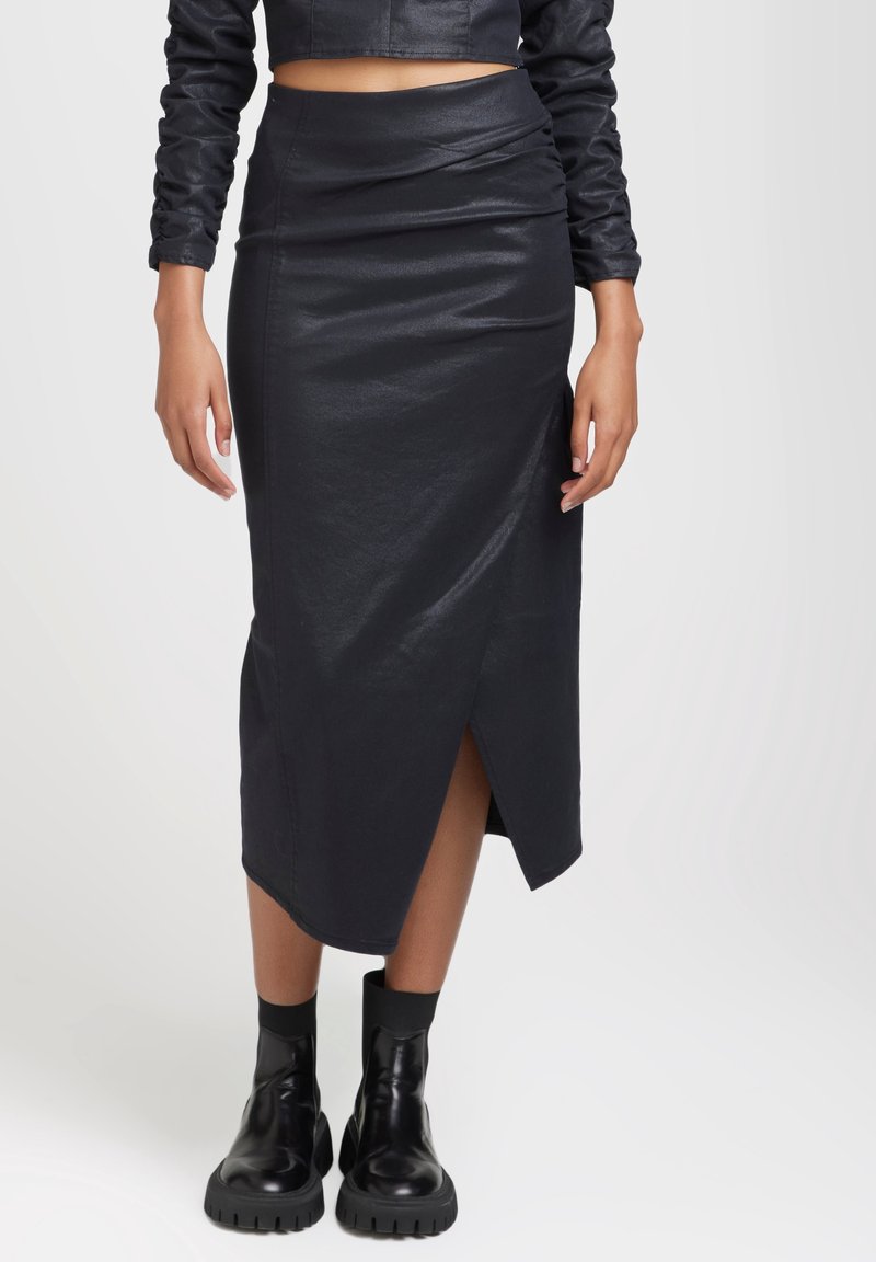 Jupe midi en simili cuir noir avec une fente à l'avant, coupe ajustée et subtil éclat. Associée à des bottines épaisses noires.