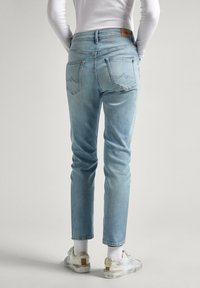 Svetlo modré denimové džínsy s stredným pásom, úzkym strihom a zadnými vreckami s diskrétnym stehom. Kombinované s bielymi teniskami a ponožkami.