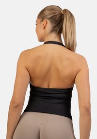 Čierny top na halterneck s hladkým povrchom, s priliehavým pásom a prekríženým dizajnom na chrbte. Kombinovaný s béžovými legínami.