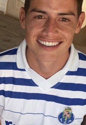 Witte trui met blauwe horizontale strepen, voorzien van een ronde kraag en het clubembleem aan de linkerkant. De persoon heeft kort haar en glimlacht.