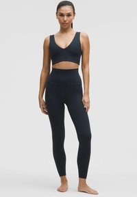 Sutien sport negru și colanți cu talie înaltă din material elastic. Topul are un design cu decolteu în V; colanții au o finisare netedă.