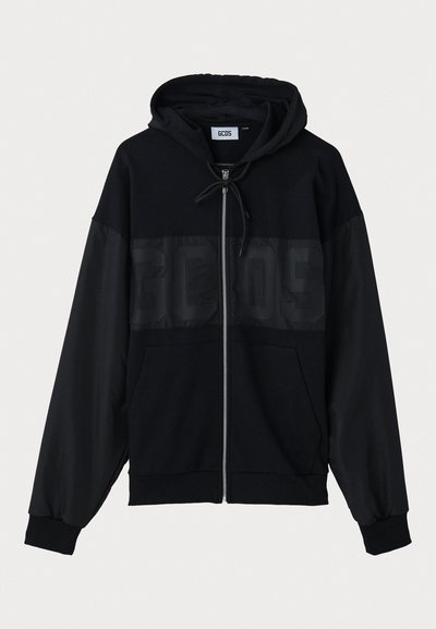 Juodas zip-up džemperis su tekstūruoto viršutinio skydelio, gaubtu, priekinėmis kišenėmis ir elastinėmis rankovėmis. Yra toninis logotipas krūtinės srityje.