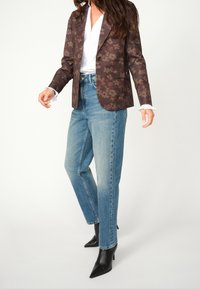 Blazer marrón con estampado floral sobre una camisa blanca, combinado con jeans rectos de pierna light blue y tacones negros de punta.