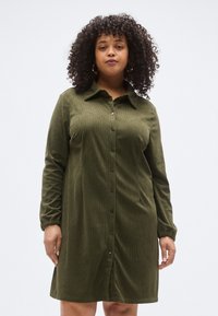 Olívazöld kordbársony ruha hosszú ujjal, gombos előrésszel és gallérral. Bordázott textúrával és laza szabással.