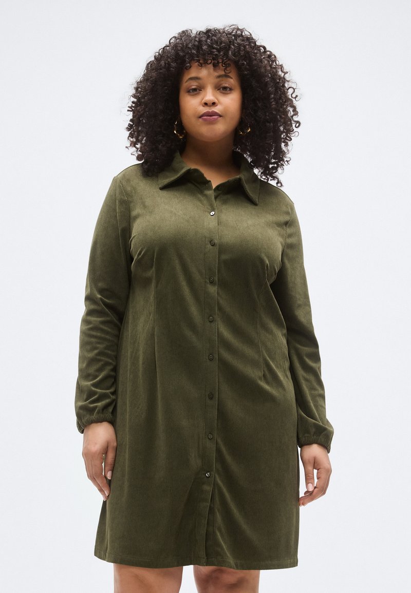 Olívazöld kordbársony ruha hosszú ujjal, gombos előrésszel és gallérral. Bordázott textúrával és laza szabással.