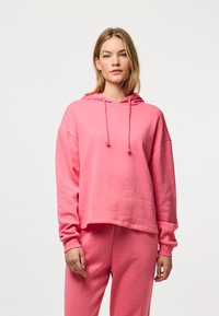 Rózsaszín kapucnis pulóver laza fit-ben, puha anyagból készült. Elől zseb, húzózsinórok és oversized ujjú kialakítással rendelkezik.