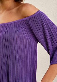 Top viola senza spalle con texture a coste e maniche ampie, con un design rilassato che enfatizza la scollatura e l'area delle spalle.