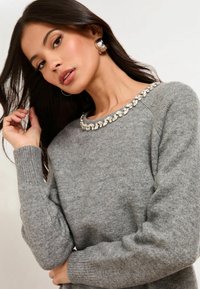 Pulover gri cu guler rotund, având un guler decorativ cu mărgele; textură moale și manșete cu nervuri, expus într-un mod casual.