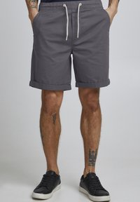 Grå bomullsshorts med rullekanter, med elastisk midje og snøring. To synlige sidelommer. Sorte sneakers brukes.