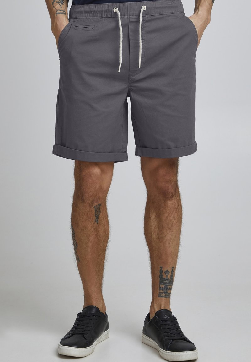 Grå bomullsshorts med rullekanter, med elastisk midje og snøring. To synlige sidelommer. Sorte sneakers brukes.