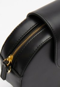 Čierna syntetická kožená taška so zaobleným tvarom, s pozláteným zipsom a detailmi šitia. Žiadne viditeľné vzory ani ďalšie akcenty.