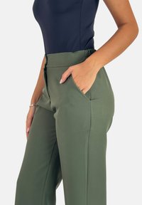 Olivgröna högmidjade byxor med en slät textur, sidofickor och en figursydd design. Tillsammans med en mörk ärmlös topp.