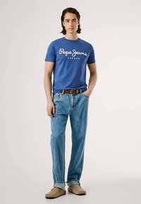 Modré bavlněné tričko s logem "Pepe Jeans London", volné světle modré džíny, hnědý kožený pásek a béžové nazouvací boty.