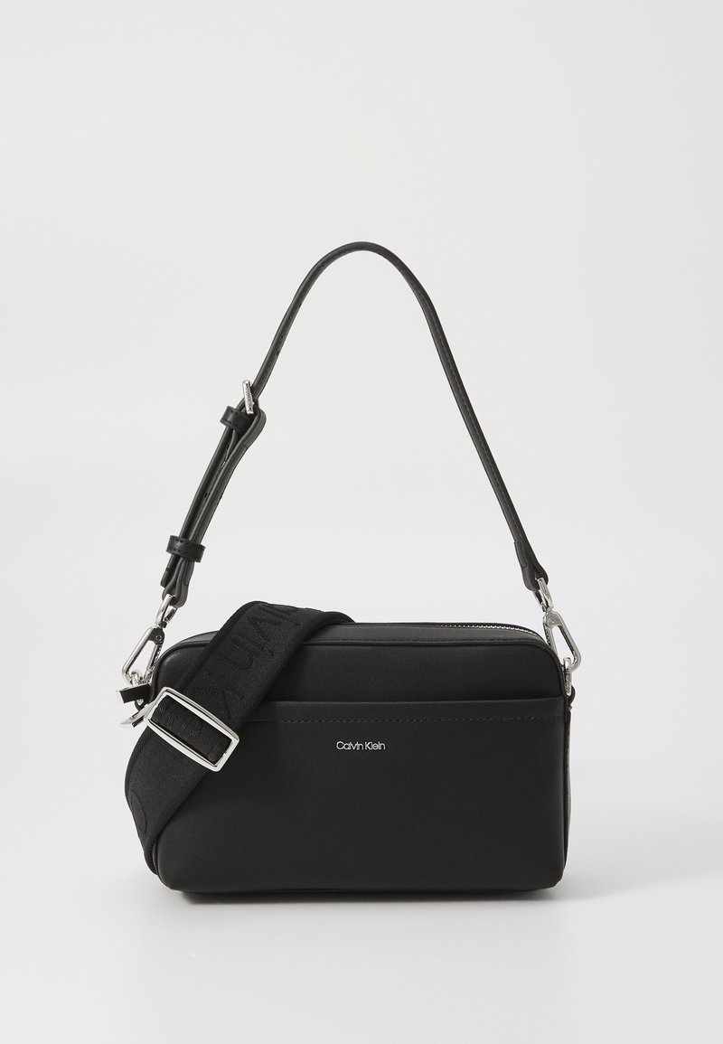 Compact black bag made of textured fabric, featuring dual straps—one leather and one fabric with logo. Silver hardware accents present.