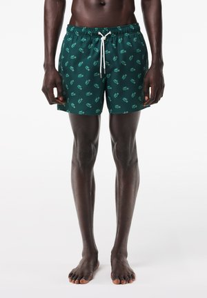 Pantalones de natación verdes con cordón blanco. Presenta un estampado de pequeñas manos en un patrón repetitivo. Hechos de un tejido ligero y de corte a la altura de la rodilla.