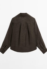 Chemise à manches longues brun foncé en tissu texturé, avec des plis dans le dos et des poignets boutonnés. Présente un col pointu et une coupe décontractée.