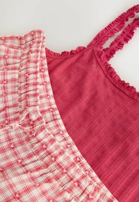 Haut rouge sans manches avec rayures texturées et bordure en dentelle, assorti à une jupe à carreaux blancs et rouges avec une taille élastique froncée.