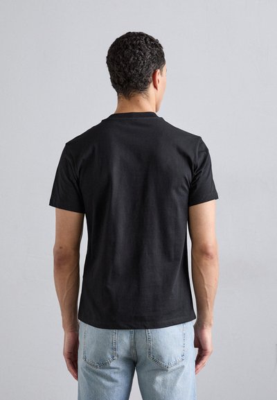 Zwarte katoen t-shirt met korte mouwen en een ronde hals, gezien van achteren, gecombineerd met lichtblauwe spijkerbroek.