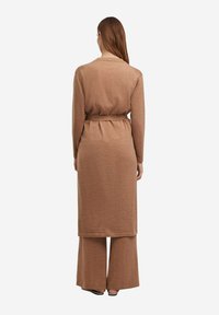 Langer, brauner Strickcardigan mit einem Bindegürtel, langen Ärmeln und geradem Schnitt, kombiniert mit weit geschnittenen, braunen Hosen. Strukturierter, weicher Stoff.