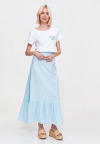 Biała krótka bluzka z niebieskim napisem "do zobaczenia wkrótce", zestawiona z jasnoniebieską, w paski, maxi spódnicą z falbanką u dołu.