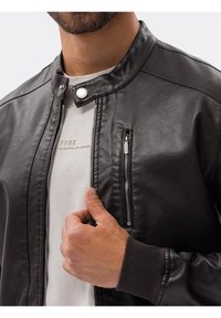 Czarna skórzana kurtka z kołnierzem zapinanym na zatrzask, przednim zamkiem błyskawicznym i boczną kieszenią; ściągacze przy mankietach; gładka tekstura i dopasowany krój.