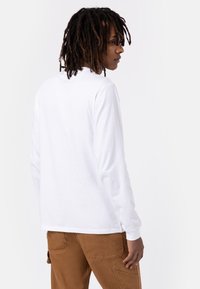Witte langetermijns t-shirt met een ronde hals, gedragen met bruine cargobroeken. Het shirt is gemaakt van een gladde, lichtgewicht stof.