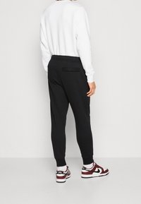 Svarta joggers med elastisk midja och en bakficka, kombinerat med vita och vinröda sneakers. Vit långärmad skjorta. Slät tygtextur.