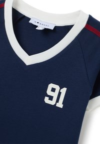 Maglietta in jersey blu marino con scollatura a V bianca, strisce rosse a contrasto sulle spalle e numero "91" bianco stampato sul davanti.