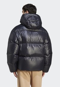 Puffjakke i glimrende sort materiale med hætte. Har et quiltet design og elastiske manchetter, der forbedrer varme og isolering.