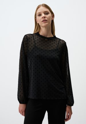 Schwarze transparente Bluse mit gepunkteter Textur, langen Ärmeln, Rundhalsausschnitt und lockerer Passform, über einem einfarbigen schwarzen Unterhemd getragen.