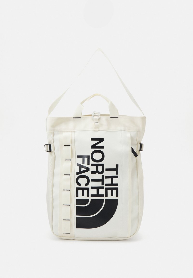 Sac à dos en tissu blanc avec logo et accents noirs. Il dispose d'une poignée supérieure, de bretelles réglables et de sangles latérales verticales.