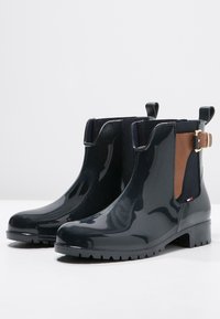 Stivali alla caviglia in gomma lucida blu navy con pannelli laterali in elastico, dettagli in pelle marrone e tacco basso; suola testurizzata per una migliore aderenza.