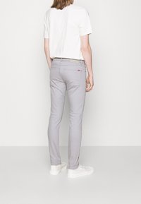 Pantalones gris slim-fit hechos de un tejido ligero, con dos bolsillos traseros, costuras sutiles, y combinados con zapatillas blancas.