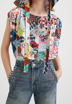 Bezrękawny wielokolorowy top typu patchwork z wstążkami, zestawiony z wysokim stanem niebieskimi jeansami z srebrnymi i czerwonymi ćwiekami.