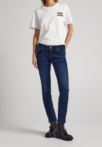 Bílý bavlněný tričko s logem "Pepe Jeans", kombinované s tmavě modrými slim-fit džíny a černými kotníkovými botami s robustní podrážkou.