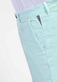 Muntgroene broek met een gladde, matte textuur. Beschikt over een zijzak en een subtiele logo-detail vlakbij de tailleband. Tailored fit ontwerp.