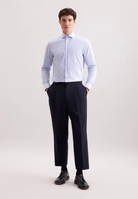 Overhemd met blauw-witte verticale strepen, gecombineerd met op maat gemaakte marineblauwe broek. Zwarte schoenen maken de outfit compleet.