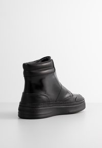 Black leather high-top sneaker with a smooth surface, padded collar, and rubber sole featuring subtle stitching and logo detailing.