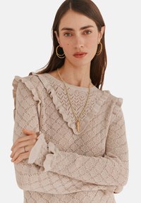 Maglione lavorato a maglia beige chiaro con un motivo a diamante testurizzato, scollatura e polsini arricciati, maniche lunghe e vestibilità comoda.